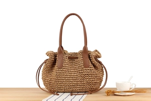 Detail einer handgewebten Stroh-Tote-Bag mit Lederriemen auf Holztisch-Arrangement