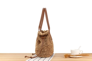Makrodetail einer handgewebten Strohtasche mit Khaki-Textur und braunem Ledergriff