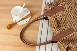 Detailaufnahme der handgewebten Strohtasche mit braunen Ledergriffen auf rustikalem Tisch