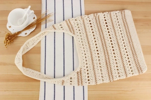Détail du sac cabas tissé crème avec rayures marron sur une table en bois clair