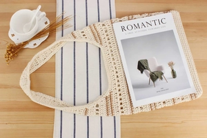 Vue à plat d'un sac cabas en crochet beige avec détails marrons sur une table bois