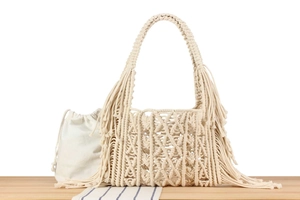 Detail of woven beige macrame tote bag with long side fringes and drawstring inner pouch
