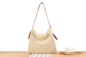 Detail of hollow crochet cotton tote bag with brown leather strap on a wooden table