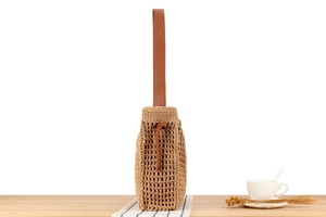 Detail of hollow woven cotton rope bag with brown leather handles on a wooden table