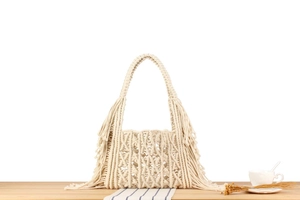 Detailed macro of handmade off-white macramé tote bag with long tassels and woven pattern