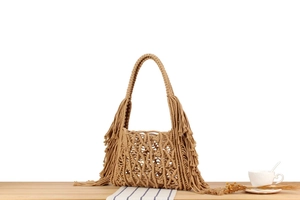 Close-up of bohemian khaki macrame hand-woven bag with fringe detail on wooden table
