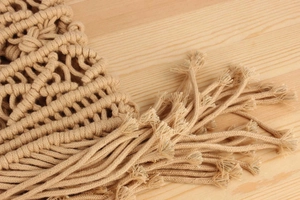 Macro detail of beige macrame weave pattern with bohemian style tassels on handmade bag