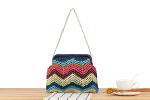 Detail of colorful hand-woven straw bag with wavy stripes and a gold metal chain strap