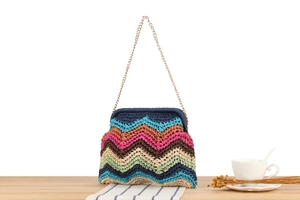Close-up of colorful zigzag woven bag with gold chain strap on a wooden table