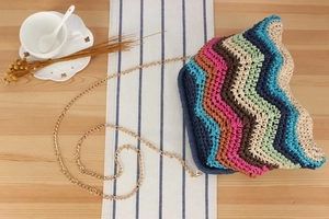 Detailed view of woven shoulder bag featuring vibrant rainbow wave patterns and gold chain
