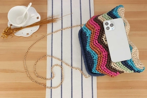 Close-up of a colorful zigzag crochet crossbody bag with a slim gold chain strap