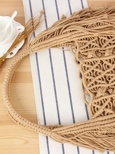 Handmade macrame woven tote bag with long tassels on a rustic wooden table setup