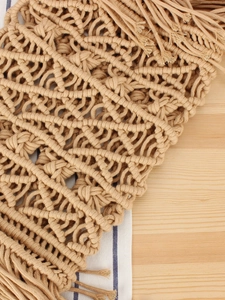 Handmade beige macramé bag with intricate knotting and fringe on a wooden background