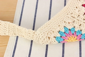 Close-up of handmade crochet bag with colorful floral patterns on beige cotton weave