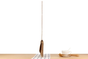 Detail of hand-woven crochet bag with a slim gold chain strap in a summer resort setting