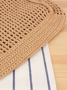 Handmade beige hollow crochet bag on wooden table with striped linen cloth