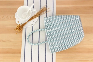 Detail view of a blue and white checkered woven basket bag on a rustic wooden table