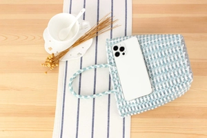 Detail of hand-woven checkered plastic tote bag showing size with a smartphone