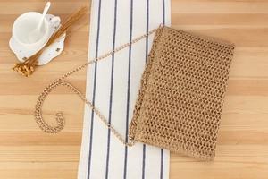 Close-up of woven crochet crossbody bag with gold chain strap on a wooden table