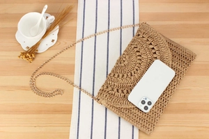 Detail of crochet straw envelope bag with gold chain strap on a wooden desk