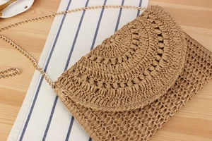 Macro view of woven crochet texture and gold chain on the beige envelope clutch bag