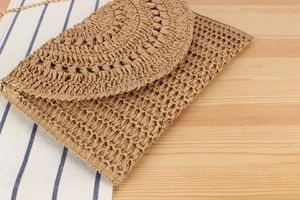 Detail of bohemian woven straw clutch with chain strap on a rustic wood surface