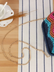 Rainbow woven shoulder bag with gold metal chain on a rustic wooden table setting