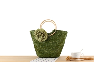 Détail du sac en paille vert olive avec poignées en bois et fleur en tissu