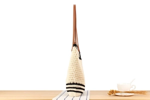 Detail of woven tote bag with black stripes and brown leather straps on a wooden table