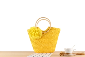 Détail d'un sac en paille tressée jaune avec poignée en bois et fleur en tissu décorative