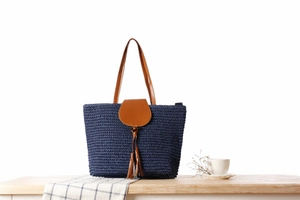 Detail of navy woven straw tote bag with brown leather handles and tassel accent