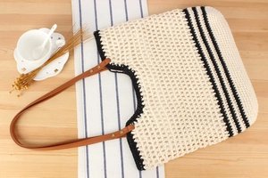 Detail of woven tote bag with black stripes and brown leather handles on wooden table