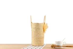 Détail d'un sac en paille tressé main avec poignées en rotin et une fleur décorative