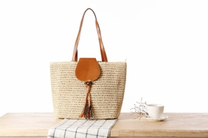 Detail view of woven paper rope tote bag with leather tassel and flap closure