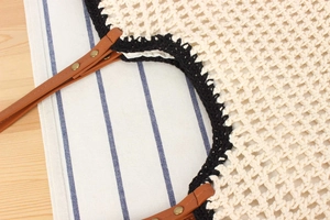 Detail of hand-woven crochet tote bag featuring leather handles and gold rivet accents