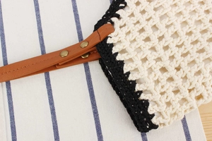 Detail of hand-woven mesh bag with black trim, leather strap and vintage rivets