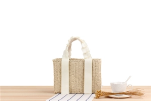 Detail of hand-woven paper rope bag with elegant white ruffled ribbon handles on a wooden table