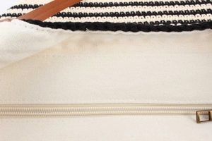 Close-up of woven handbag interior with beige canvas lining and metal zipper closure