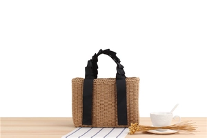 Detail of straw woven handbag with black pleated satin handles and natural texture