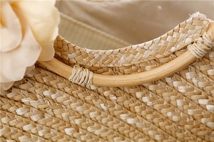 Détail d'un sac à main en paille tressée avec poignée en rotin et accents floraux
