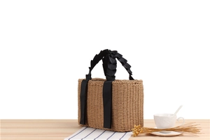 Close-up of woven straw tote bag with black pleated handle on a wooden table setup