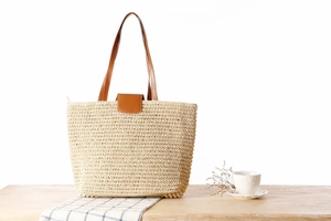 Detailed close-up of woven paper rope texture and brown leather straps on a summer tote