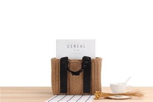 Detail view of coffee brown woven straw tote with black satin ribbon handle on wooden surface
