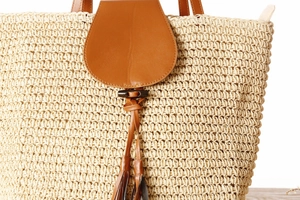 Detail of paper straw woven bag with brown leather flap, fringe tassel and wooden buckle