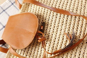 Detail of paper rope woven bag featuring brown leather flap and vintage wooden toggle closure
