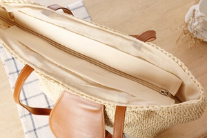 Detail of hand-woven straw tote bag featuring brown leather straps and inner zipper closure