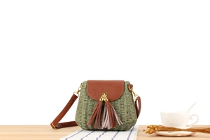 Détail d'un sac tressé vert avec rabat en cuir marron, longues franges et fermoir doré