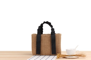 Detail of hand-woven straw tote bag featuring elegant black ruffled ribbon handles