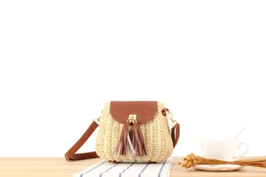 Détail d'un sac bandoulière beige tissé avec pompons en cuir marron et boucles dorées