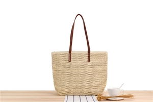 Detail of hand-woven straw tote bag with brown leather handles for summer beach travel